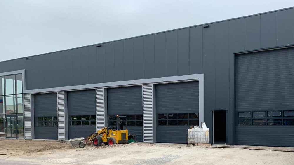 Grijze overheaddeur met beglazing en elektrische aandrijving. Elzinga bedrijfsdeuren techniek